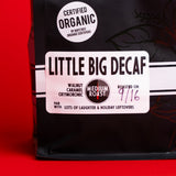 A bag of Fresh Roasted Coffee's 'Little Big Decaf' medium roast coffee, featuring a black bag with a white label, set against a solid red background.