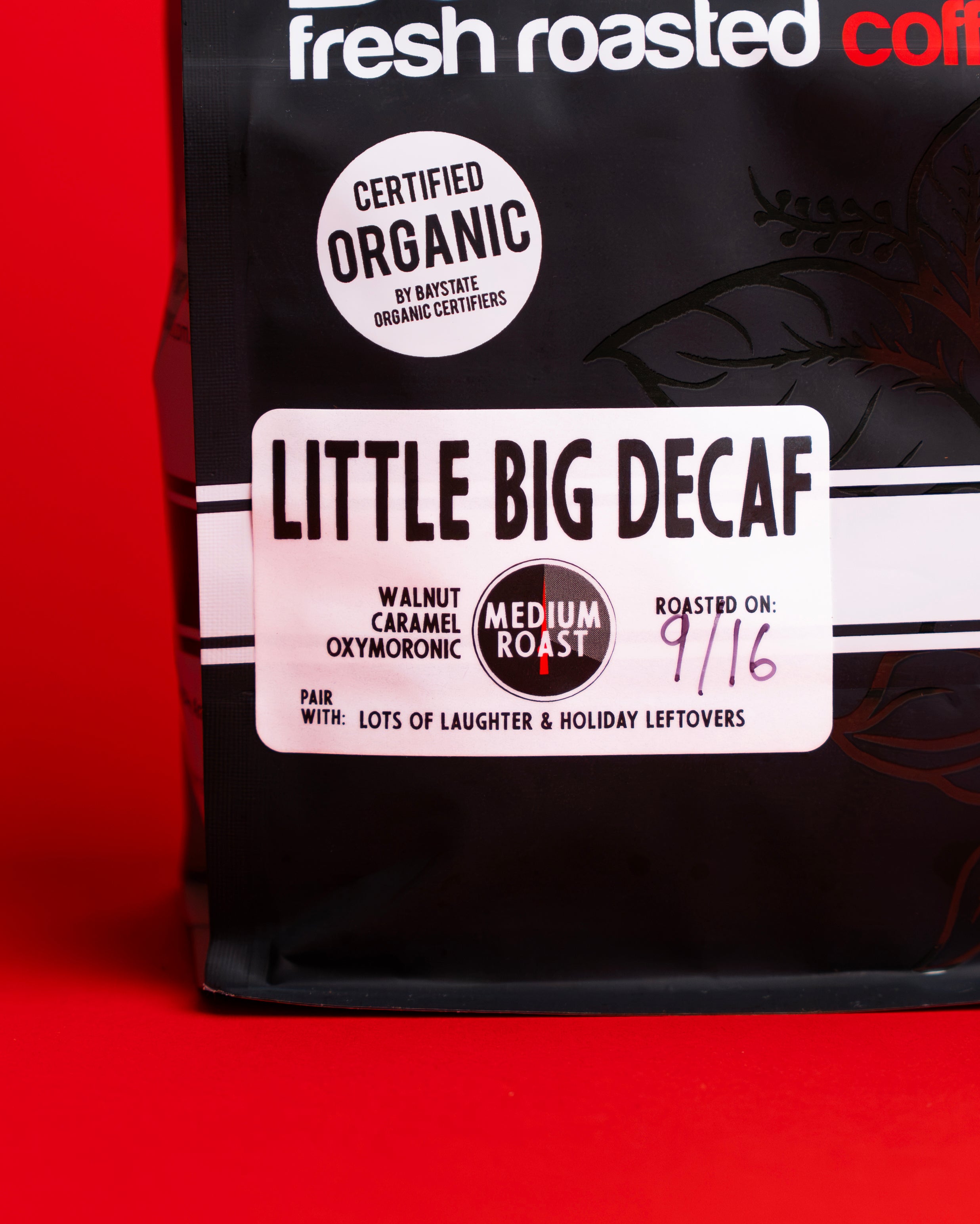 A bag of Fresh Roasted Coffee's 'Little Big Decaf' medium roast coffee, featuring a black bag with a white label, set against a solid red background.